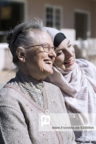 Lächelnde Seniorin und Betreuerin vor dem Haus