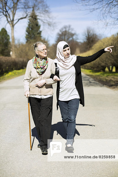 Volle Länge der häuslichen Betreuerin  die der älteren Frau beim Gehen auf der Straße etwas zeigt.