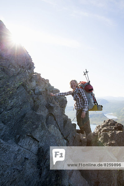 Porträt einer glücklichen Kletterin die auf Felsen gegen den Himmel steht.