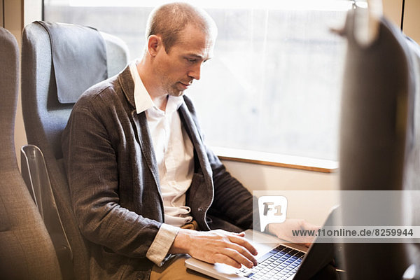 Mature businessman using laptop in train