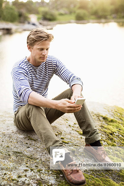 Volle Länge des Mannes Textnachrichtenübermittlung durch Handy auf Felsen am Seeufer