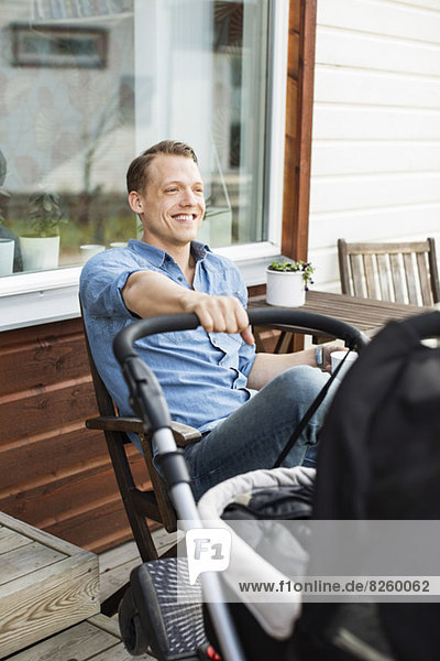 Happy man with baby carriage sitting at patio