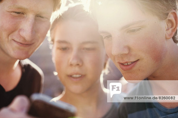 Junge männliche Freunde beim gemeinsamen Lesen von Textnachrichten auf dem Handy im Freien