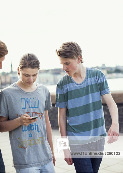 Junge Männer  die beim Gehen auf dem Bürgersteig gemeinsam mit dem Handy telefonieren
