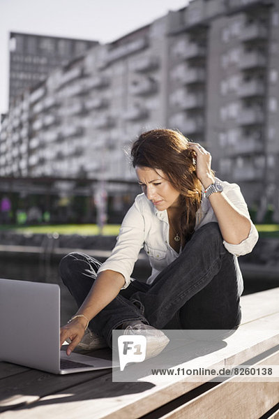 Businesswoman using laptop while sitting on boardwalk