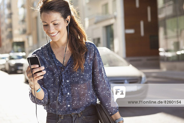 Glückliche Geschäftsfrau mit dem Handy beim Musikhören auf der Straße