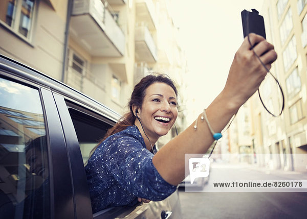 Glückliche Geschäftsfrau beim Fotografieren durchs Handy aus dem Autofenster auf der Straße