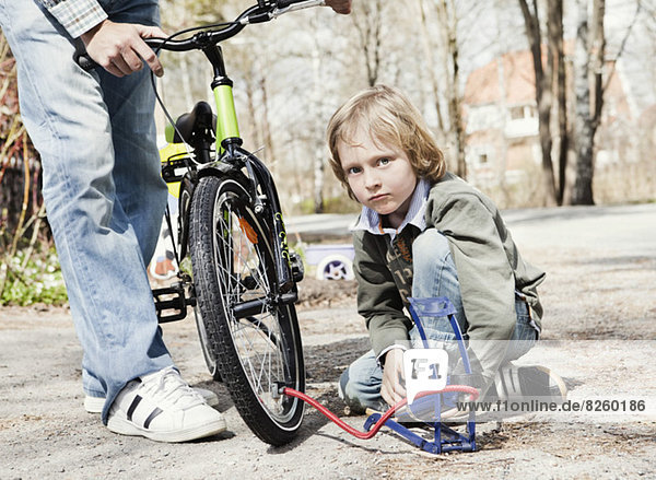 Portrait of boy filling bicycle tire with foot pump while father standing on road