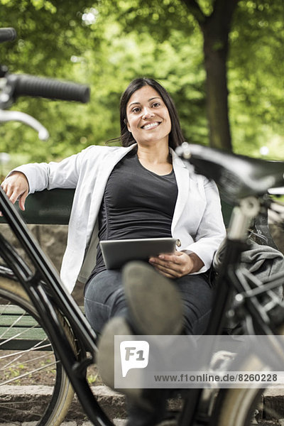 Businesswoman with digital tablet smiling while relaxing on park bench