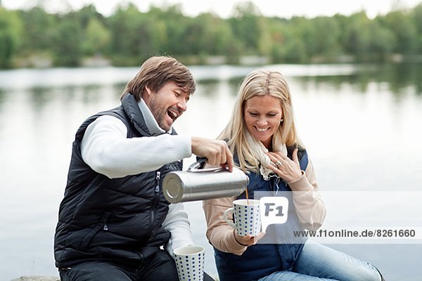 Couple sitting by lake with hot coffee