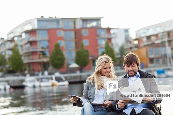 Couple sitting by water and reading newspaper