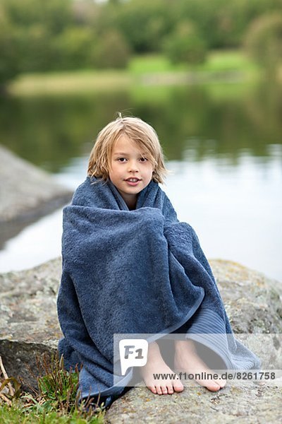 Portrait of boy wrapped in towel sitting by lake