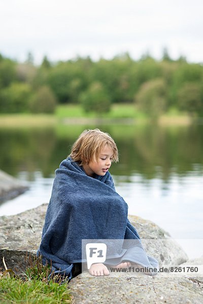 Portrait of boy wrapped in towel sitting by lake