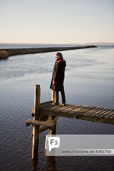A senior woman standing on a jetty by the sea  Sweden.