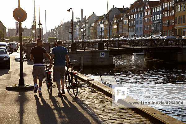 Two men walking with their bicycles against the light  Denmark.