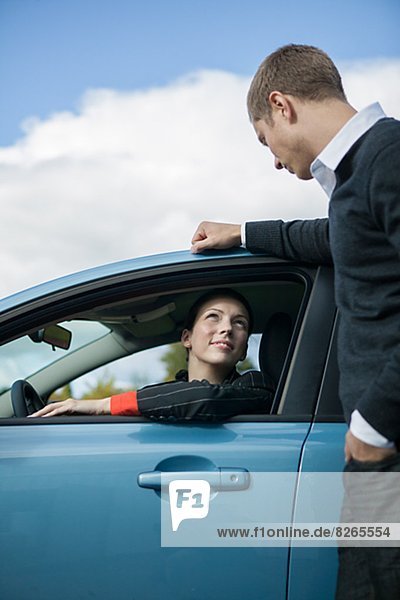 Young woman sitting in car and talking with man