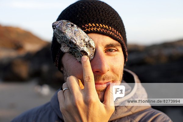 A man poses for a portrait while coving his eye with a shell in Fort Bragg  California.