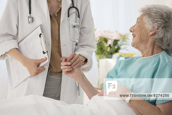Arzt und alternder Patient halten sich im Krankenhaus an den Händen