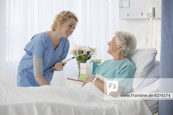 Nurse and aging patient talking in hospital room