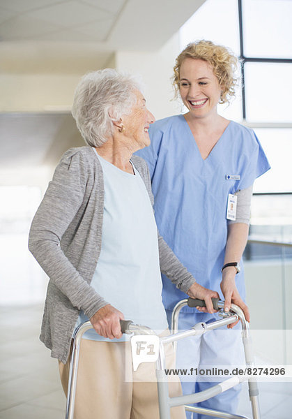 Seniorenpatientin mit Spaziergängerin lächelt Krankenschwester im Krankenhausflur an