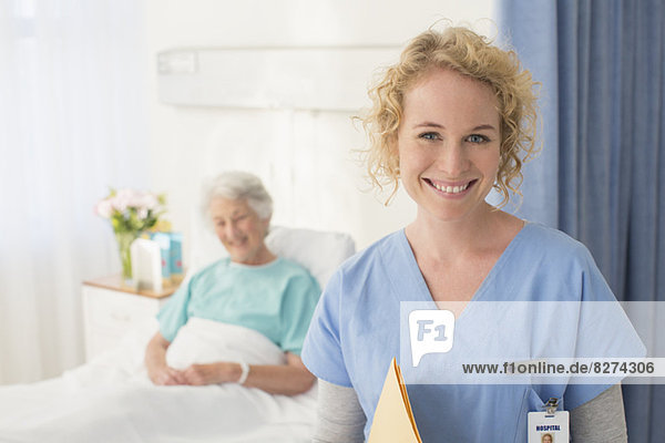 Porträt einer lächelnden Krankenschwester mit einem älteren Patienten im Hintergrund