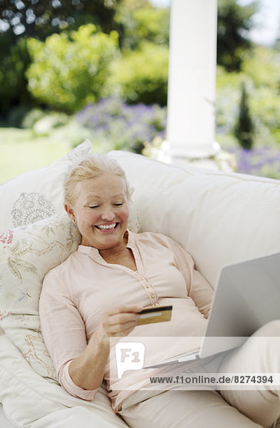 Seniorenfrau beim Online-Shopping auf dem Terrassensofa