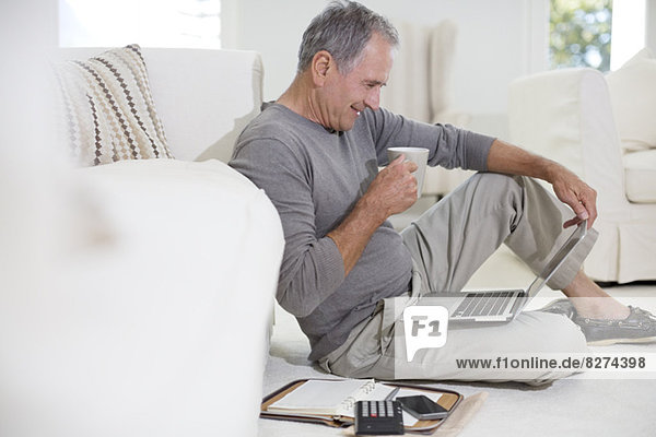 Senior Mann mit Laptop auf dem Wohnzimmerboden