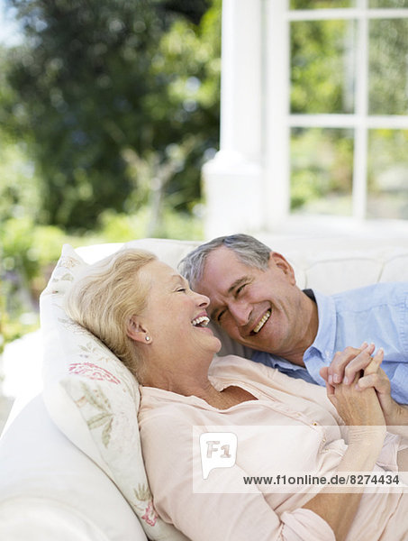 Seniorenpaar,  das auf dem Sofa auf der Terrasse liegt und Händchen hält.
