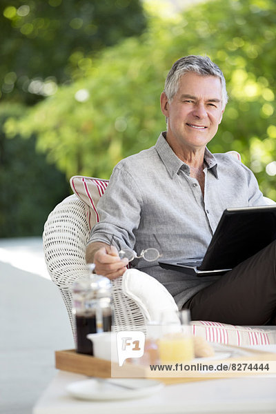 Senior Mann mit Laptop auf der Terrasse