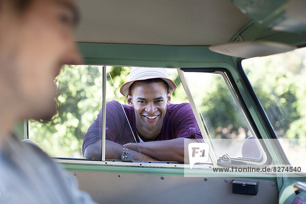 Lächelnder Mann  der sich auf das Fenster des Wohnmobils stützt.