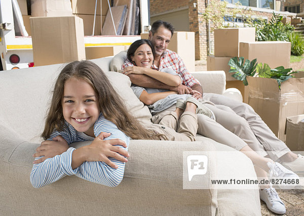 Portrait of smiling family on sofa in driveway near moving van