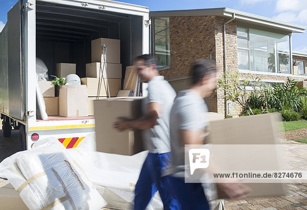 Movers carrying cardboard boxes in driveway