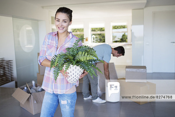 Portrait of smiling woman holding potted plant in new house