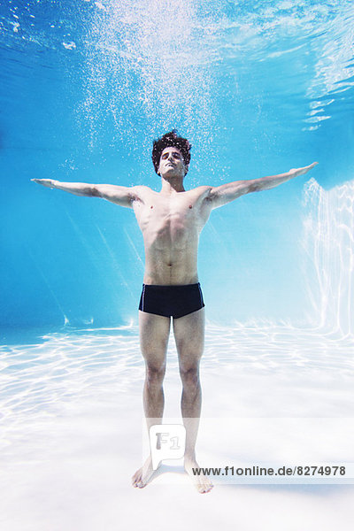 Mann steht unter Wasser im Schwimmbad mit ausgestreckten Armen