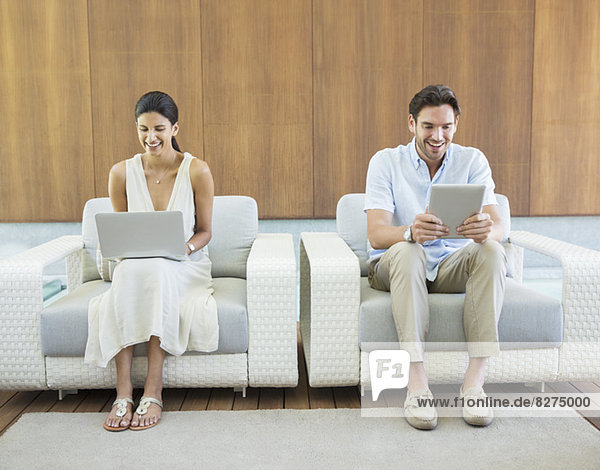 Couple using laptop and digital tablet in armchairs