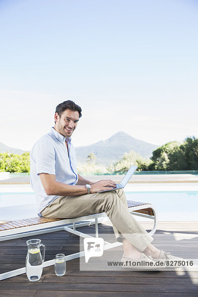 Mann mit Laptop auf dem Sessel am Pool