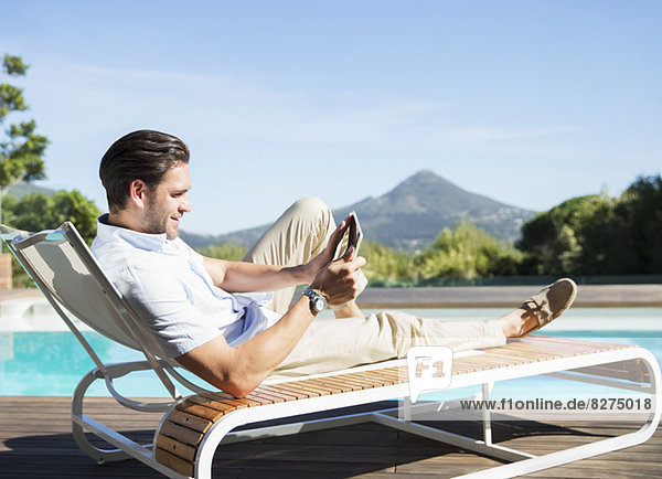 Man using digital tablet on lounge chair at poolside