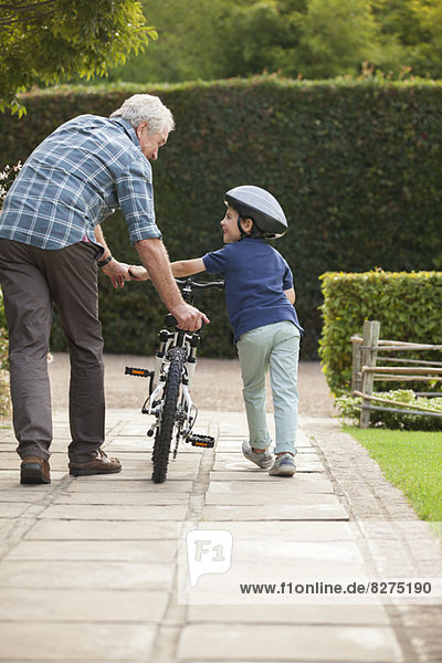 Grandfather and grandson pushing bicycle on sidewalk