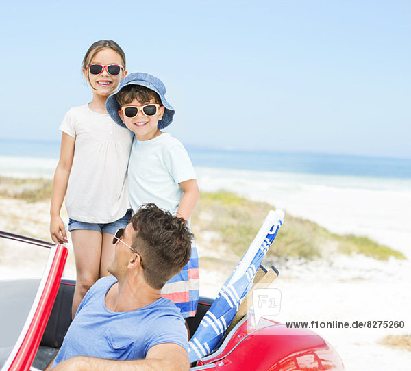 Father and children smiling in convertible at beach