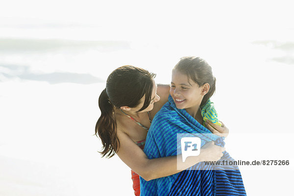 Mutter wickelt Tochter in Handtuch am Strand ein