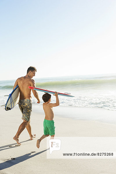 Father and son carrying surfboard and bodyboard on beach