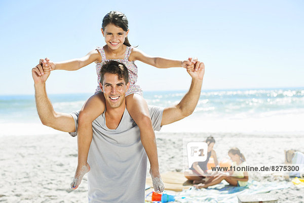 Father carrying daughter on shoulders at beach