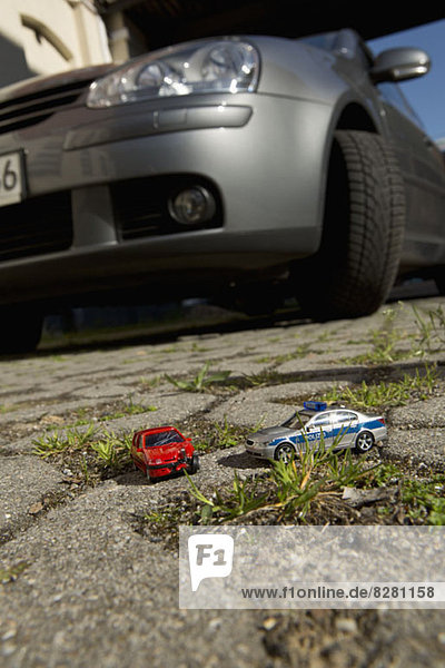Ein Spielzeugauto-Crash mit einem Spielzeug-Polizeiauto  echtes Auto im Hintergrund