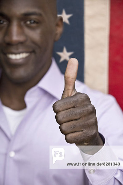 Happy man giving 'thumbs up' in front of American flag