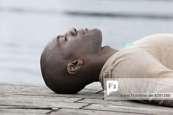 Man napping on decking by lake
