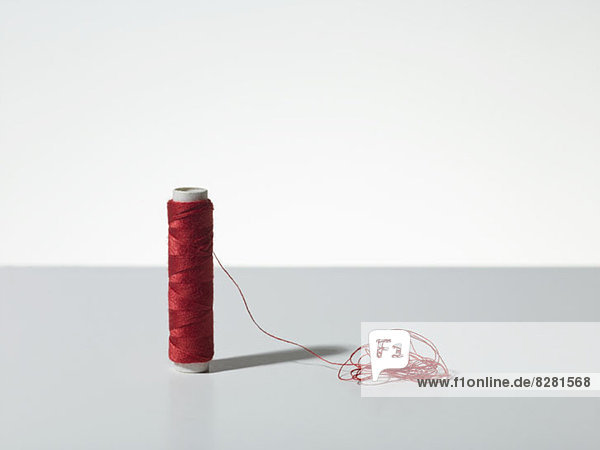 Eine Spule aus rotem Garn mit einem Haufen verwirrter Fäden.