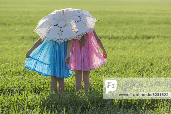 Zwillingsschwestern stehen auf einem sonnigen Feld unter einem Schirm