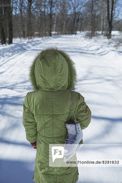 Ein junges Mädchen steht auf einer verschneiten Straße mit einem Schlittschuh über der Schulter.