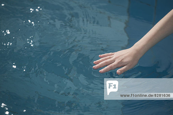 Die Hand eines jungen Mädchens  die das Wasser in einem Schwimmbad kräuselt.