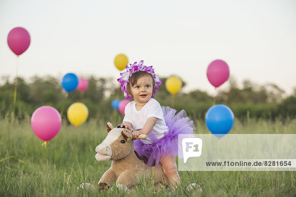 Ein kleines Mädchen mit Tutu auf einem Schaukelpferd in einem Feld mit Ballons
